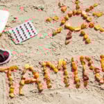 The words vitamin D is written in the sand on the beach out of orange gummies.