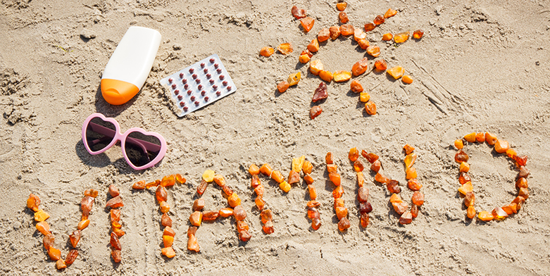 The words vitamin D is written in the sand on the beach out of orange gummies.