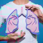A woman is holding a paper cut out of her lungs in front of her chest.