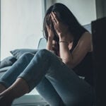 A woman is sitting on the floor with her head in her hands.