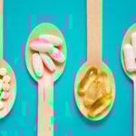 Four wooden spoons filled with different types of pills on a blue background.