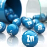 A blue tub with Zn laying on its side with a bunch of blue balls with Zn on them rolling out.