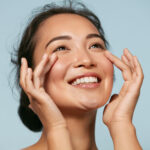 A woman is smiling and touching her face with her hands.