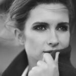 A black and white photo of a woman covering the bottom half of her face with the top of her jacket.