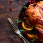 A roasted turkey on a plate with oranges and cranberries