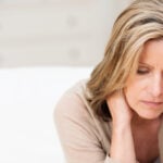 A woman is sitting on a couch looking concerned with her head in her hands.