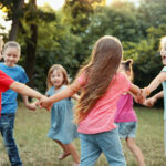 A group of children are holding hands in a circle in a park.
