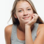 A young girl is smiling, resting her chin on her hand.