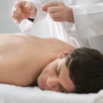 A man is laying on a table getting acupuncture in his back.