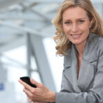 A woman is sitting down, smiling while holding a cell phone.