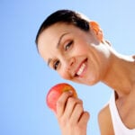 A woman is smiling while holding an apple in her hand.